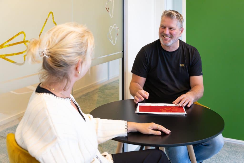 man op kantoor aan tafel in gesprek met vrouw
