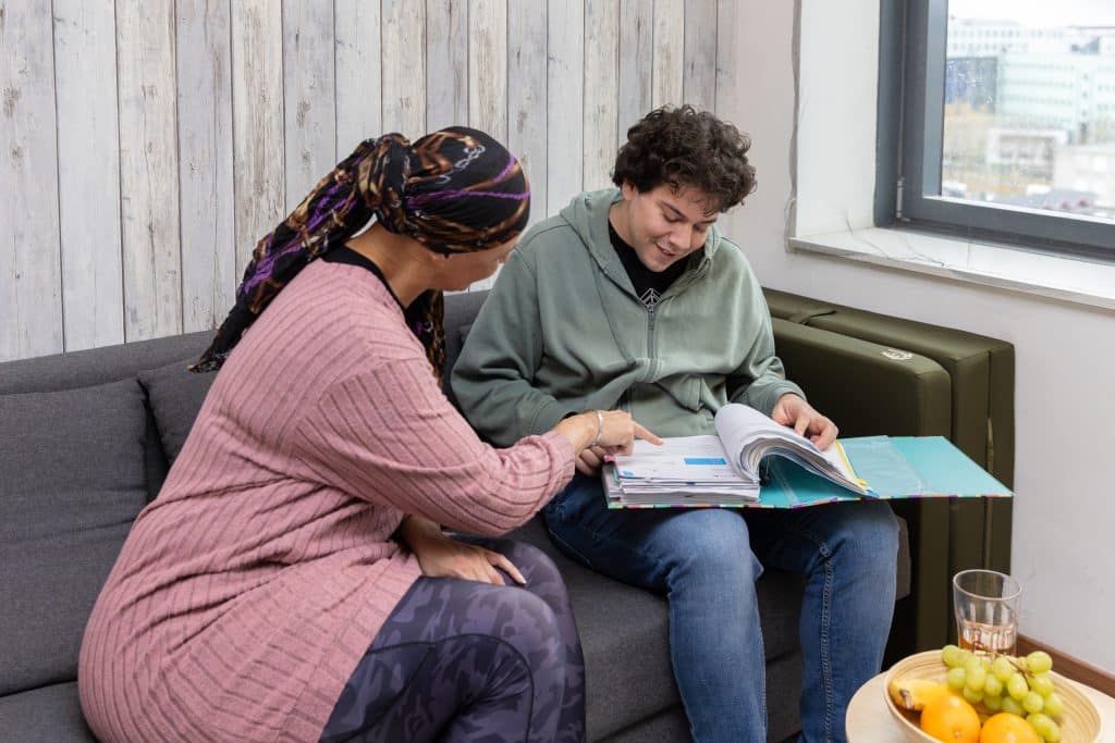 vrouw helpt jongeman op bank die in een map kijkt