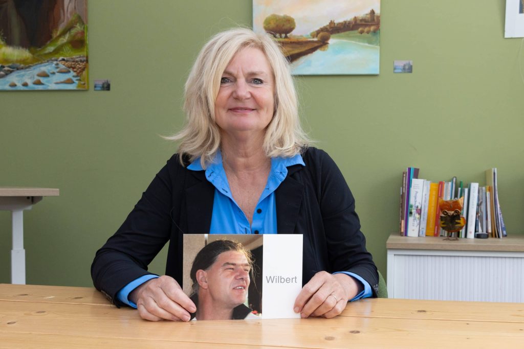 Kitty zit aan tafel en houdt foto van Wilbert vast