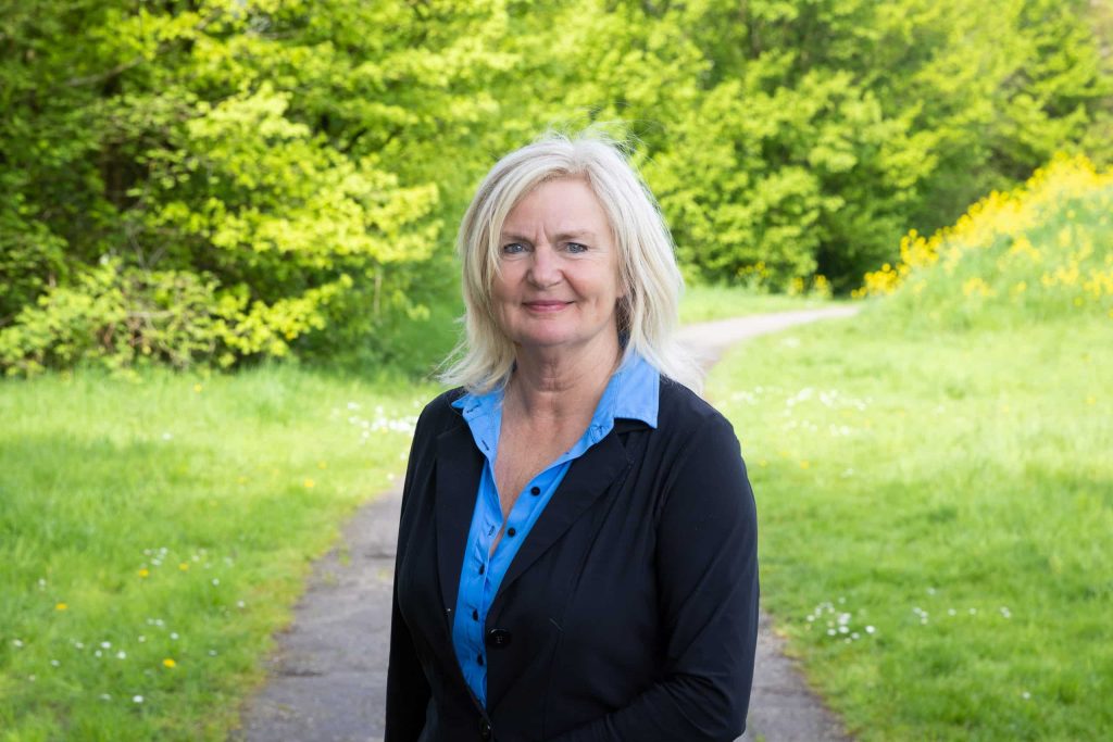 Portretfoto Kitty met lichtgroen gras en bomen achter haar