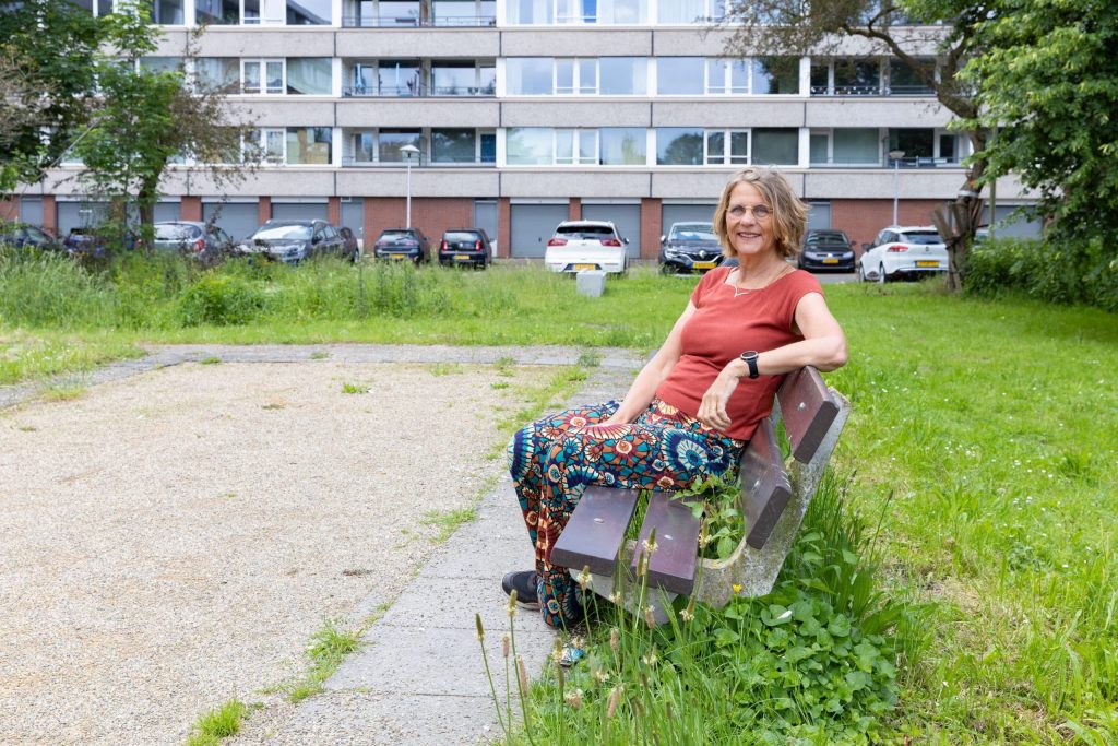Karin Kraaij zit op een bankje voor een flatgebouw