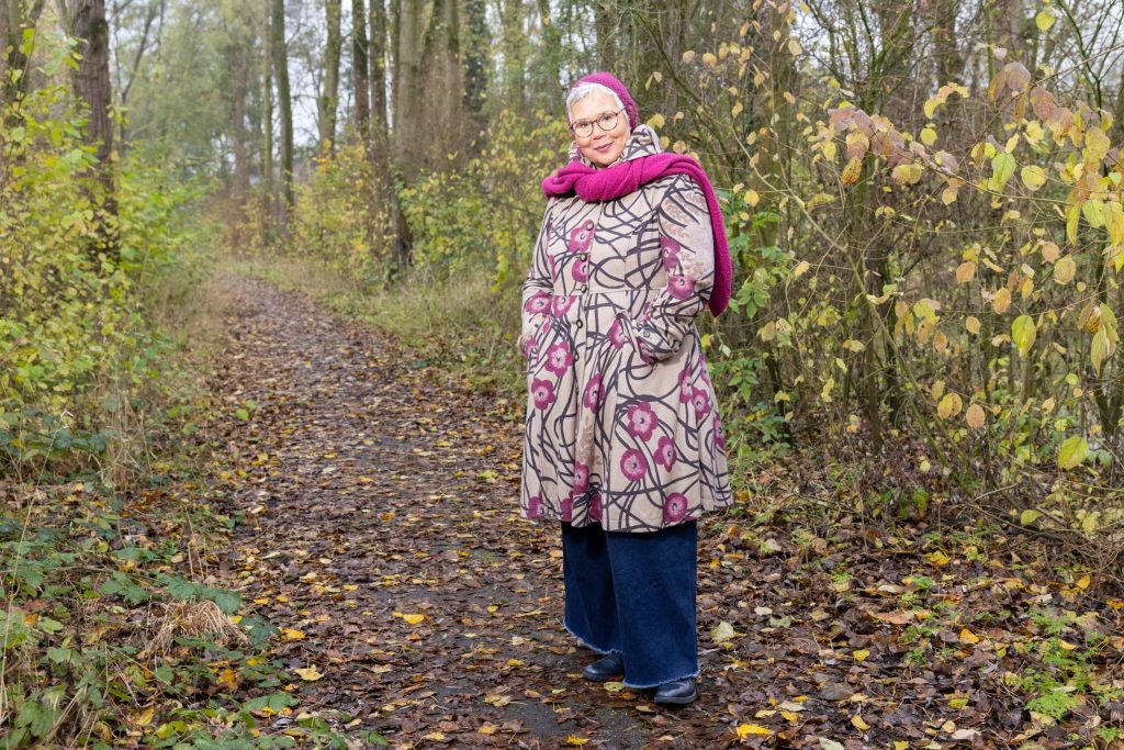 Annemiek Baudoin staat met een fleurige jas in het bos
