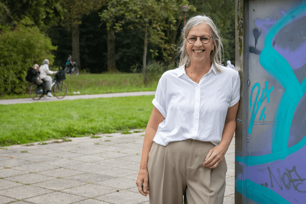 Evelien Roos leunt met hand tegen muur met gras en bomen in de achtergrond